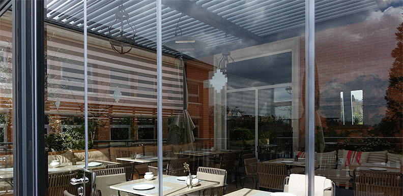 cubierta de lamas de aluminio orientables cubriendo terraza de restaurante con corninas de vidrio